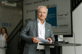 Mann steht auf der Bühne und spricht zum Publikum